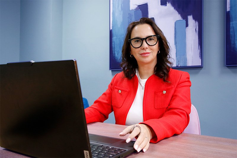 Professional portrait of Alina Butnariu Sildan, ACCA-qualified accountant and founder of AA&R Certified Accountants, sitting at a desk in a modern office environment.